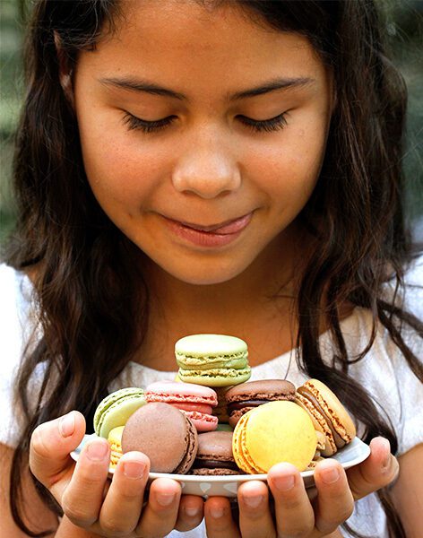 Smiling girl holding colorful macarons, symbolizing the brain’s reward response to taste anticipation.