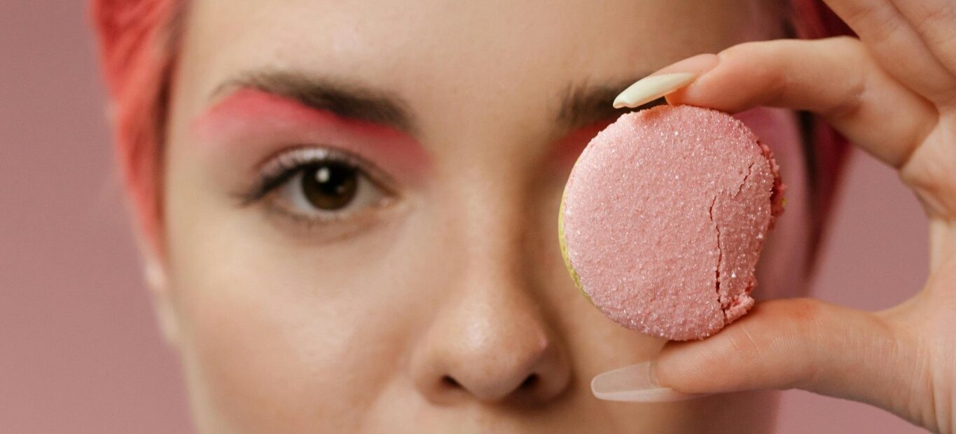 Pink macaron held to the eye, showing how color sets sweetness expectations before the first bite.