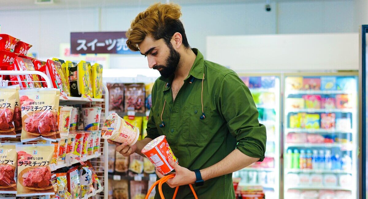 Shopper in Japanese snack aisle comparing products, choosing named regional flavors over Asian-inspired.